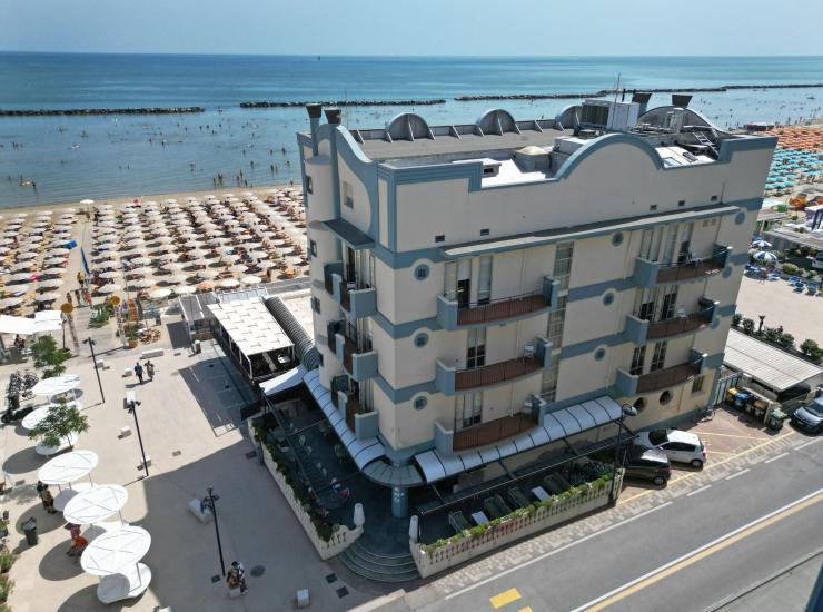 Spiaggia affollata, mare calmo, hotel moderno, ombrelloni ordinati.